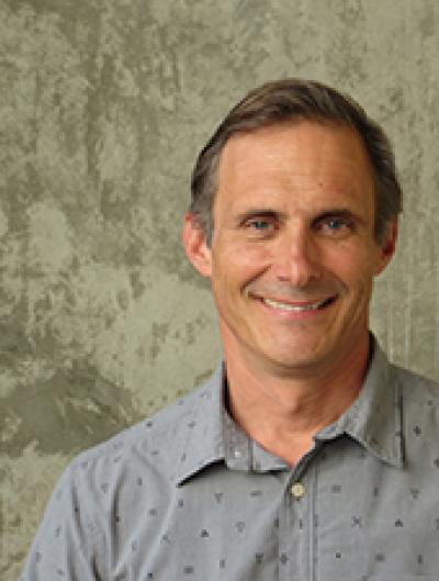 Matt smiling, wearing a gray shirt over an earth-tone background