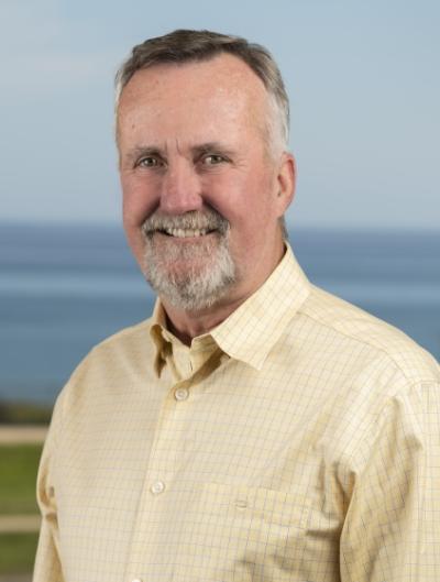 Steve smiling on Decker's Deck. Yellow shirt with a view of the Pacific Ocean behind him