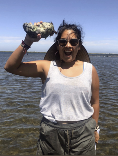 Lilli, knee-deep in water, holding a mollusk of some kind