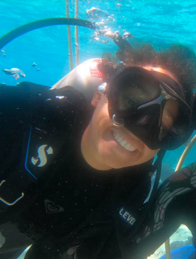 Olivia diving underwater with scuba gear, wetsuit, and a big smile